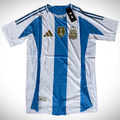 Camiseta titular de fútbol Adidas de Argentina para la temporada 2024/25, con franjas celestes y blancas, y escudos oficiales.