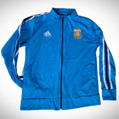 Campera frizada Adidas en color celeste con el escudo de la AFA y franjas blancas en las mangas.