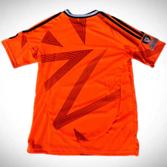 Camiseta de fútbol suplente del Real Madrid 2024/25, de color naranja con diseño de líneas negras en la parte posterior.