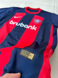 Camiseta de fútbol de San Lorenzo, temporada 2024/25, con diseño en rojo y azul, logo de Nike y etiqueta de autenticidad.