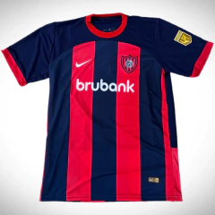 Camiseta titular de San Lorenzo 2024/25, con diseño a rayas azul marino y rojo, logo de Nike y patrocinador Brubank.