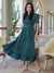 Vestido longo verde com detalhes em renda, modelo elegante e feminino, usado por uma mulher em ambiente interno iluminado.