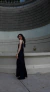 Modelo luciendo un vestido de satén negro con escote en V, de pie frente a una pared decorativa.