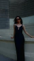 Mujer posando con un vestido negro de satén con escote en V, usando gafas de sol, en un entorno arquitectónico moderno.