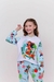Pijama infantil de manga longa e calça com estampa da Moana, usada por menina sorridente em fundo claro