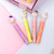 Quatro marca-textos coloridos com tampas de coelhinho, em cores rosa, amarelo, roxo e laranja, sobre um fundo de papel colorido.