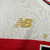 Detalhe do logo dourado em camisa branca com faixa vermelha do São Paulo FC