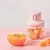 Mini processador de alimentos recarregável rosa com cubos de frutas ao lado de uma tigela de suco de laranja.
