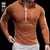 Camiseta esportiva masculina de manga comprida na cor laranja, com detalhe de zíper na gola e ajuste ao corpo.