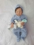Bebê reborn super realista Lucca, vestido com macacão azul e chapéu, segurando um brinquedo de pelúcia.