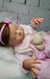 Doll bebê reborn super realista Laura vestindo roupinha rosa e segurando um brinquedo