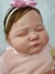 Bebê reborn super realista Bianca com cabelo castanho e laço rosa, vestindo uma blusa rosa.
