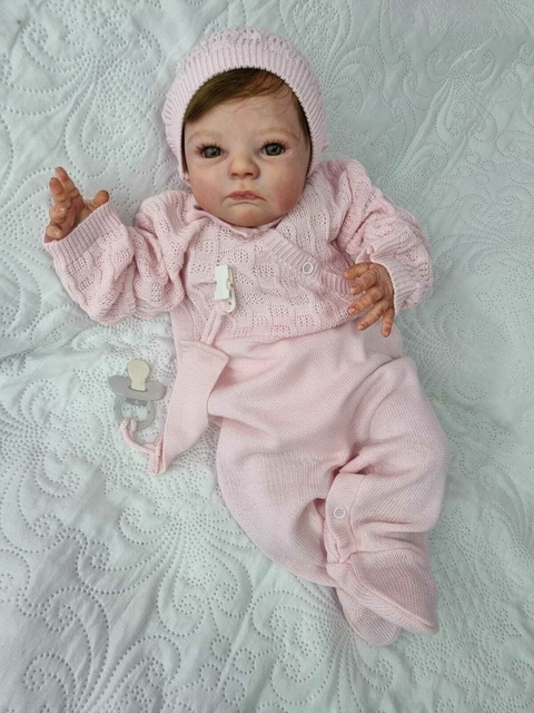 Bebê reborn super realista Anabel vestindo um macacão rosa e boné, com expressão serena e detalhes realistas.