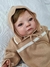 Boneca Bebê Reborn super realista Miguel vestindo um suéter com capuz, com olhos verdes e expressão suave.