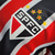 Detalhe do escudo da camisa do São Paulo FC, destacando as cores preta, vermelha e branca, e as estrelas douradas.