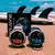 Dois smartwatches Brave GPS resistentes à água 5ATM ip69k exibidos na areia da praia com pranchas de surf ao fundo
