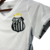 Camisa feminina branca do Santos, modelo 24/25, com o escudo do time e detalhes em preto.