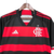 Camisa do Flamengo I 24/25, modelo torcedor, nas cores preta e vermelha, com detalhes em branco, pendurada em um cabide.