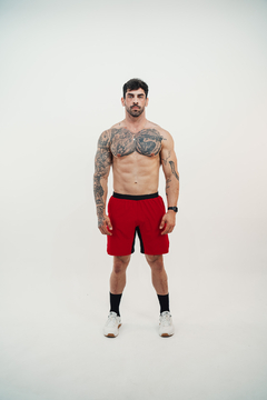 Homem musculoso usando shorts vermelhos Lurk, com tatuagens visíveis, em fundo branco.