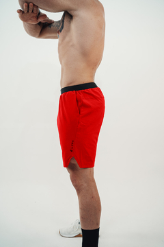 Modelo usando shorts vermelhos Lurk, com detalhe da cintura preta, em fundo neutro.