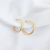 Brinco argola tubo trançado em ouro 18K, com design elegante e brilho intenso, sobre um fundo de tecido branco.