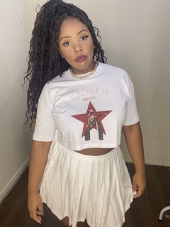 Modelo usando uma camiseta cropped branca com estampa e saia branca, destacando um estilo moderno e ousado.