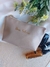 Necessaire sintética personalizada em tom bege com nome dourado "Dra. Silvia", ao lado de produtos de beleza e flores decorativas. Ideal para brinde de luxo