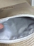 Necessaire de material sintético em tom bege com zíper branco aberto, mostrando o interior forrado em tecido cinza claro.