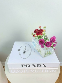 Livro caixa grande da Louis Vuitton com estampa Monograma em um fundo claro com livro caixa prada e caixa vaso acrilico