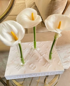 Livro caixa grande da Louis Vuitton com estampa Monograma em um fundo claro com vaso 3 tubos de vidro e flores naturais decorando a sala