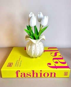 Vaso trouxinha em murano marfim com flores tulipas brancas permanentes artificiais em cima de um livro verde intitulado "fashion".