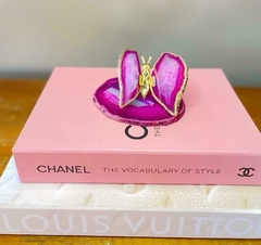 Livro caixa grande da Louis Vuitton com estampa Monograma em um fundo claro e borboleta de ágata rosa