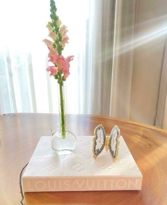 Livro caixa grande da Louis Vuitton com estampa Monograma em um fundo claro e borboleta de ágata rosa e vaso tubo balão pequeno