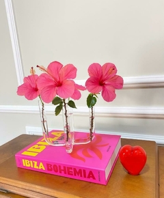 Livro caixa Ibiza grande com capa rosa e detalhes em amarelo e vermelho e vaso 4 tubos em vidro com murano ao lado decorando a sala
