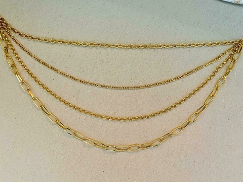 Cinto Correntes com várias camadas de correntes douradas sobre um fundo claro.