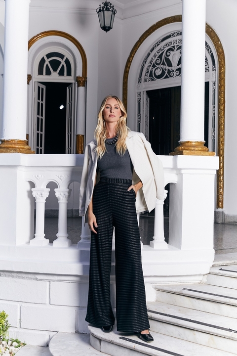 Modelo usando a calça Alara, com um blazer claro e blusa cinza, em um ambiente elegante.