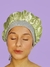 Touca de cetim na cor verde claro com faixa de ribana, usada por uma mulher com os olhos fechados, em fundo roxo. para noite de sono confortavel e cabelos sem frizz de manhã