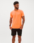Homem sorridente usando uma camiseta laranja e shorts pretos, com tatuagens visíveis nos braços.