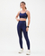 Mulher usando um top trilobal azul eclipse, combinando com leggings, em um fundo neutro.