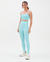 Mulher usando um top e leggings na cor azul celeste, com tênis claros, em fundo branco.