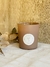 Vela Bruna visón en recipiente de vidrio mate, con etiqueta blanca y decoraciones naturales a su alrededor.