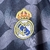 Emblema do Real Madrid em bordado, com a coroa acima, em um fundo azul com detalhes em amarelo e branco.