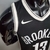 Camiseta regata preta e branca do Brooklyn Nets, com logo da Nike, vista lateral em um manequim.