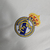 Logotipo bordado do Real Madrid em um fundo branco, representando o kit infantil da equipe.