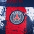 Detalhe do logo do Paris Saint-Germain em uma camisa pré-jogo azul e vermelha da Adidas.