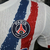 Camisa branca do Paris Saint-Germain com detalhes em vermelho e azul e o logo do clube.