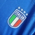 Emblema da Seleção Italiana de Futebol em um uniforme azul, com estrelas acima e as cores verde, branco e vermelho representando a bandeira da Itália.