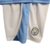 Detalhe do kit infantil do Manchester City, com as cores azul e branco e o emblema do clube.