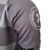 Detalhe da manga da camisa masculina cinza da Mercedes para a temporada 23/24 da Fórmula 1, exibindo o logo de campeão.