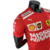 Camisa masculina vermelha da Ferrari da temporada 23/24 de Fórmula 1, exibindo logotipos de patrocinadores.